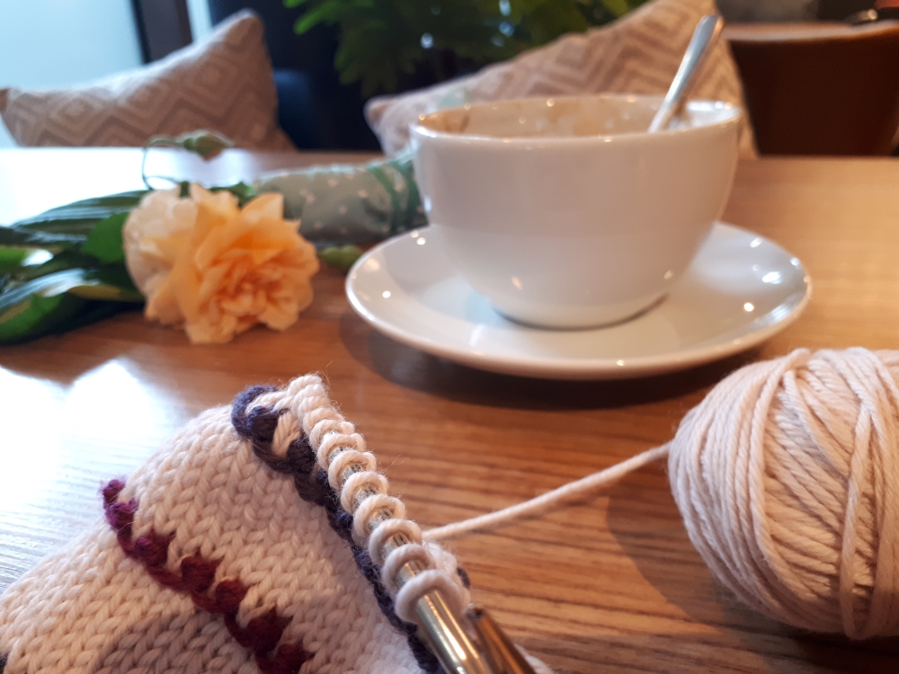 Knitting, coffee mug and flower on a table in a café