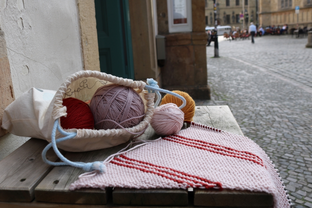 knitting started for the Tattoo shawl and wool balls in a jute bag on a small table by a cobblestone street