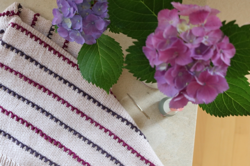 An unconspicuously mended childern's sweater on a table with flowers