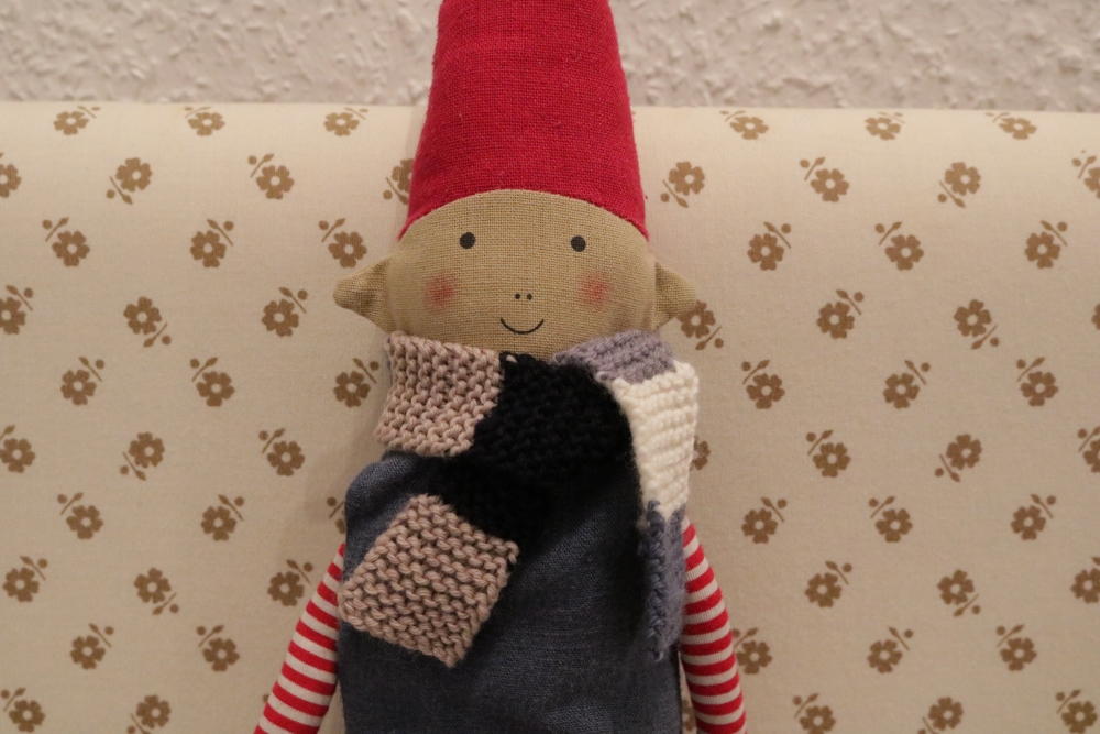 An elf rag doll wearing a knitted scarf with broad stripes