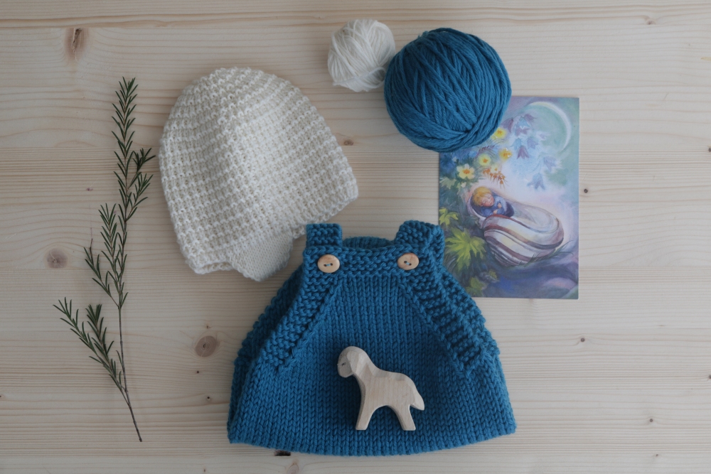 White baby bonnet and blue romper suit with flowers and greeting card