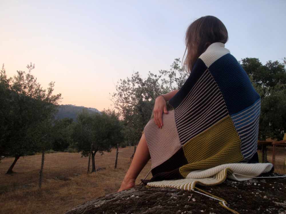 Sitting woman wrapped in a home-knitted woollen blanket in the middle of the Portuguese countryside